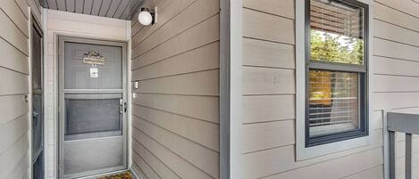 A house entrance with a door, a window with blinds, and a welcome mat.