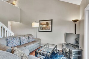 Un salon avec un canapé, une table basse, un téléviseur et un tableau encadré au mur.