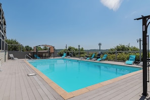 Une piscine rectangulaire avec une terrasse en bois, entourée de chaises longues bleues et d’un espace salon abrité.