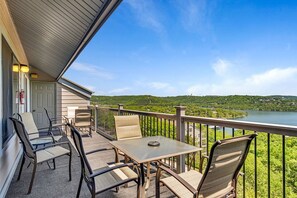 Un balcon avec une table et des chaises, donnant sur un lac et une végétation luxuriante.