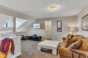 Uma sala de estar moderna com televisão, sofá, mesa de centro e escada para um andar superior.