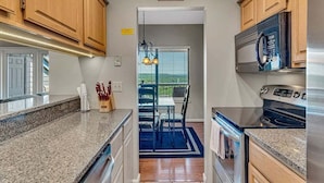 Een keuken met houten kasten, granieten aanrechtbladen, roestvrijstalen apparatuur en een eethoek met een blauw tapijt.