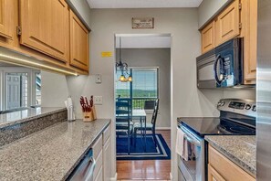 A kitchen with wooden cabinets, granite countertops, stainless steel appliances, and a dining area with a blue rug.