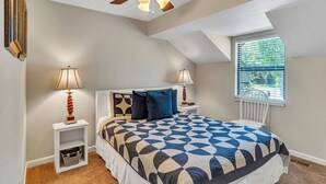 A bedroom with a sloped ceiling, a bed with a geometric patterned bedspread, two bedside tables with lamps, a window with blinds, and a ceiling fan. - Incredible Lake Views, Boat Slip Included, 3 Bedrooms & Free Tickets Near Silver Dollar City (Branson)