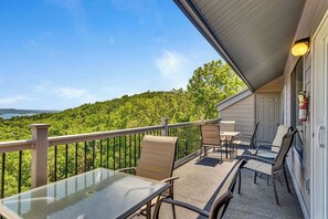 Un balcon avec une table et des chaises en verre, donnant sur une zone boisée.