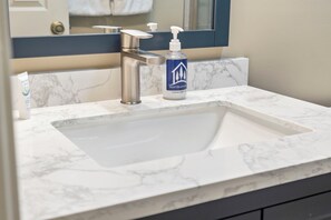 Un lavabo de salle de bain avec un plan de toilette en marbre, un robinet moderne et un distributeur de gel hydroalcoolique.