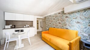 Un espace de vie compact comprenant un coin cuisine, un coin repas avec des chaises blanches et un canapé.