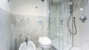 Une salle de bain avec un sol en marbre, une douche en verre, des toilettes blanches et un bidet.