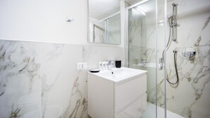 A modern bathroom with a white marble sink, a glass shower enclosure, and a large mirror. - Italianway - The B Village Standard - 03 (Milan)