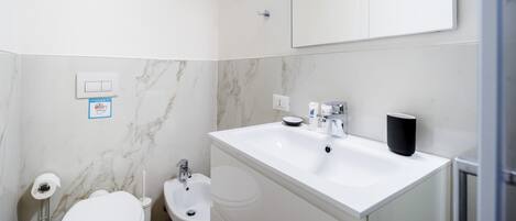 Une salle de bain moderne avec un lavabo blanc, un bidet, des toilettes et un miroir au-dessus du lavabo.