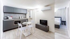 A modern kitchen with a dining area, a flat-screen TV, and a separate bedroom with a bed and nightstand. - Italianway - The B Village Standard - 03 (Milan)