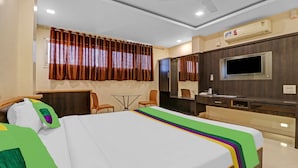 Habitación de hotel con cama, escritorio, silla, televisor y aire acondicionado.