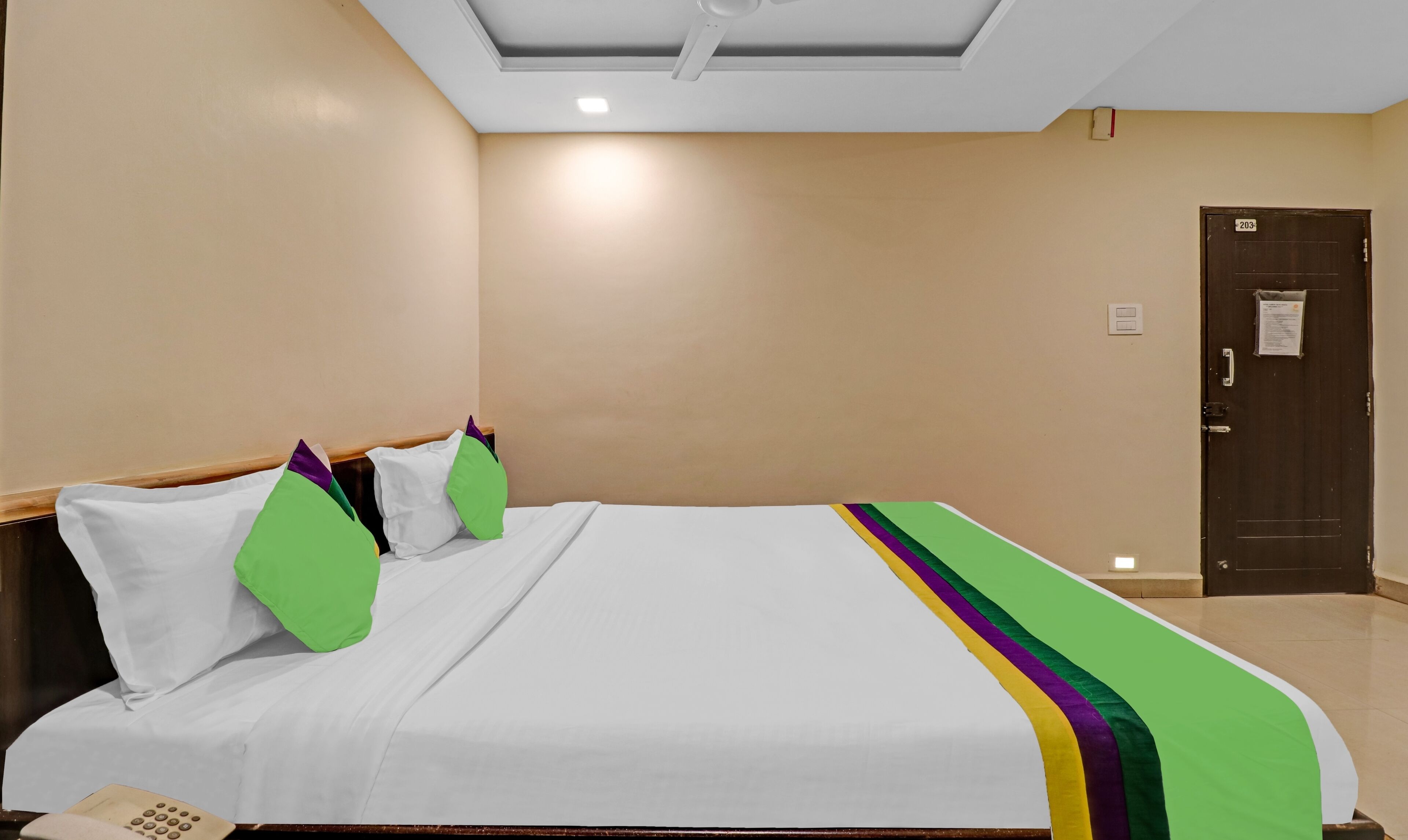 A hotel room with a large bed, a wooden headboard, and a door with a number sign.