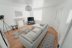 A modern living room with a grey sofa, a fireplace, a TV, and a large window. - Spacious home close to city centre, tram, hospitals, universities, Peak District (Sheffield)