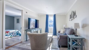 Et hotelværelse med fjernsyn, sofa, stol, skrivebord og lampe.