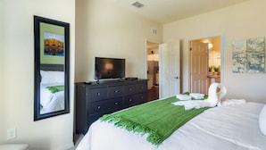 Un dormitorio con cama, cómoda, televisor y obras de arte en las paredes.