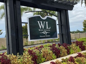 A sign for West Lucaya Village Resort with a view of landscaped gardens and a palm tree.