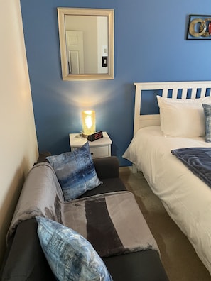 Relax in a stylish bedroom with a comfortable bed, sofa, and bedside table, featuring a mirror and artwork.