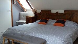 Ett sovrum med ett sluttande tak, en säng med ett geometriskt mönstrat överkast, två kuddar, ett sängbord med en lampa och en bänk vid fotändan av sängen.