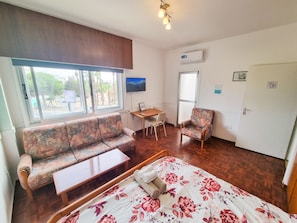 A room with a bed, a sofa, a chair, a small table, and a TV. - Gardenrooms Larnaca (Larnaca)