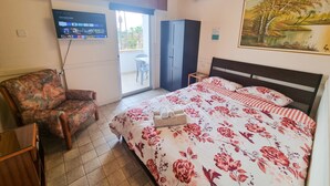 Una habitación de hotel con una cama, una silla, un televisor montado en la pared, aire acondicionado y un cuadro en la pared.