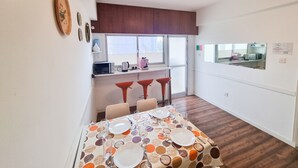 Comedor con una mesa dispuesta para cuatro personas, cocina con ventanal y espejo que refleja la cocina.