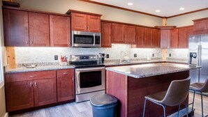 Una cocina moderna con armarios de madera, electrodomésticos de acero inoxidable, encimera de granito y una zona de bar con dos taburetes.