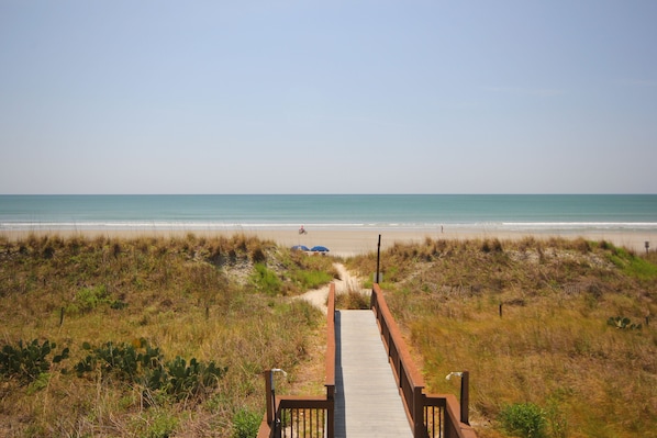 A wooden boardwalk leading to a beach with a clear view of the ocean.