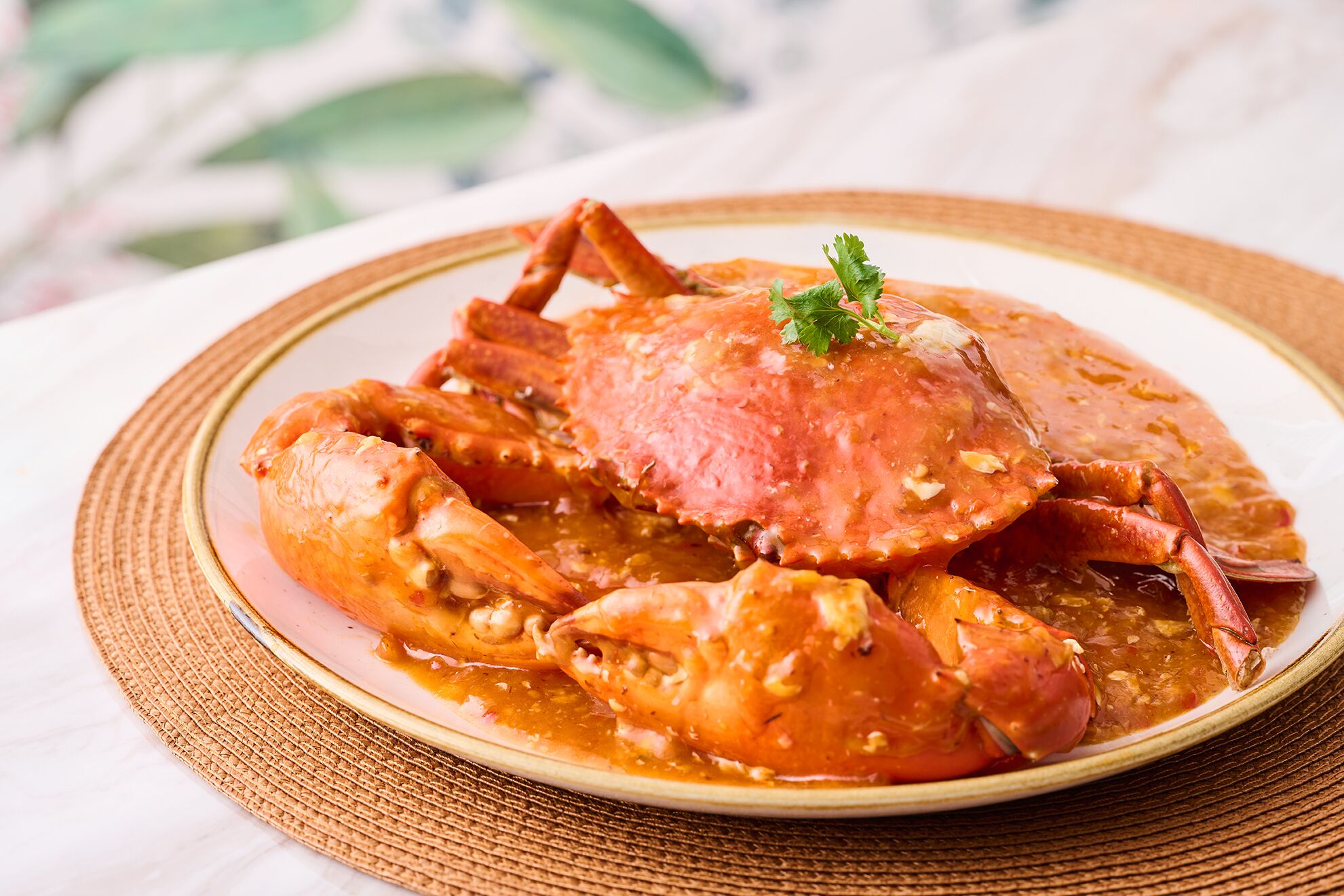 A plate of crab with sauce, garnished with a leaf, on a woven mat.