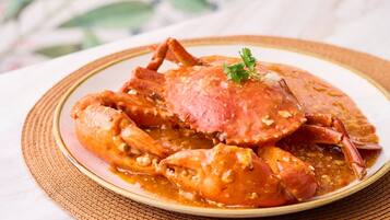 A plate of crab with sauce, garnished with a leaf, on a woven mat.