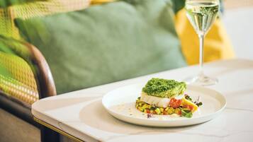 A plate with a dish on a table, a glass of white wine, and a green cushion in the background.