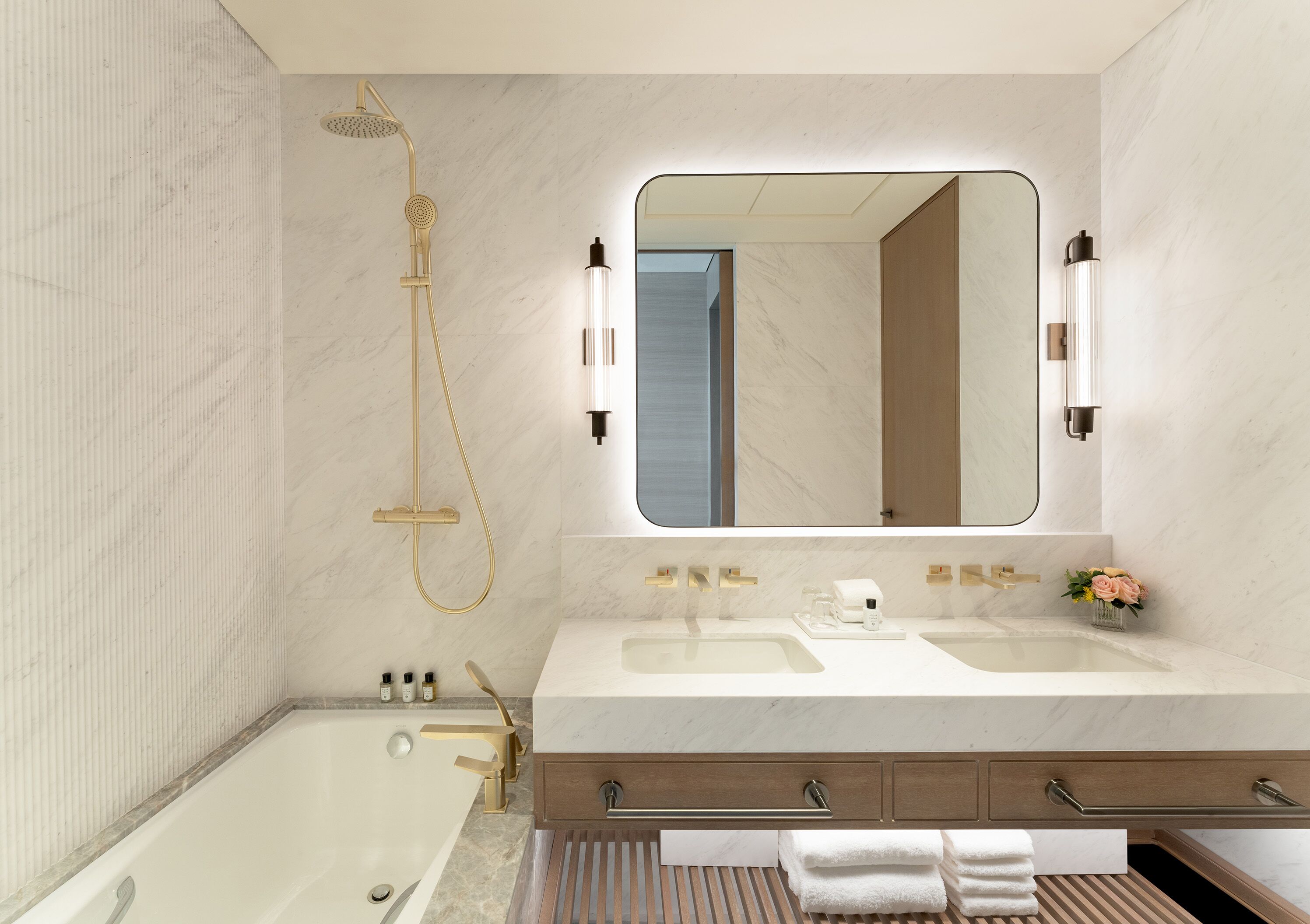 Un baño moderno con bañera, dos lavabos, un mueble de tocador con cajones, un espejo grande y un cabezal de ducha.