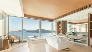 A modern spa room with a large window overlooking a body of water and mountains.