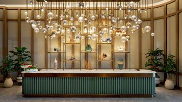 A reception area with a green reception desk, hanging spherical light fixtures, and potted plants.