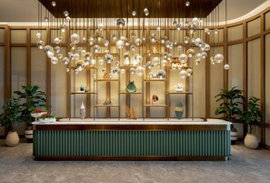 A reception area with a green reception desk, hanging spherical light fixtures, and potted plants. - The Fullerton Ocean Park Hotel Hong Kong (Hong Kong)