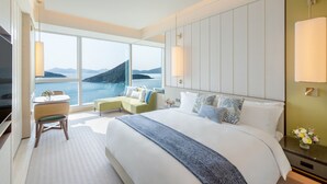 A modern hotel room with a large bed, a seating area with a view of the sea, and a television.