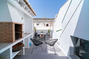 Un petit patio extérieur avec une cheminée en briques, une table avec des chaises et une pergola offrant de l’ombre.