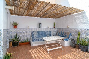 Ein überdachter Patio-Bereich mit Tisch und Bänken, Blumentöpfen und einer gefliesten Wand mit blauem Muster.