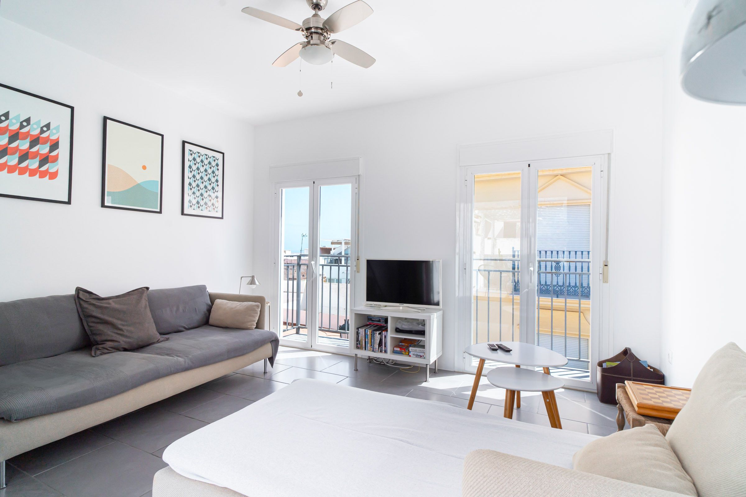 A modern living room with a sofa, a flat-screen TV, a coffee table, and a balcony with a view.