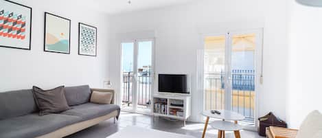 A modern living room with a sofa, a flat-screen TV, a coffee table, and a balcony with a view.