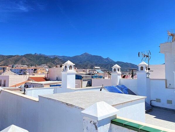 Un toit-terrasse avec un bâtiment blanc, une petite tour et une montagne en arrière-plan.