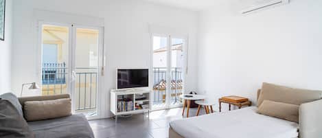A modern living room with a sofa, a TV on a stand, a ceiling fan, and a balcony with a railing.
