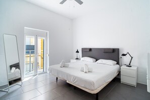 Une chambre d’hôtel moderne dotée d’un grand lit, de deux tables de chevet avec lampes, d’un ventilateur de plafond et d’une porte-fenêtre coulissante donnant sur un espace extérieur.