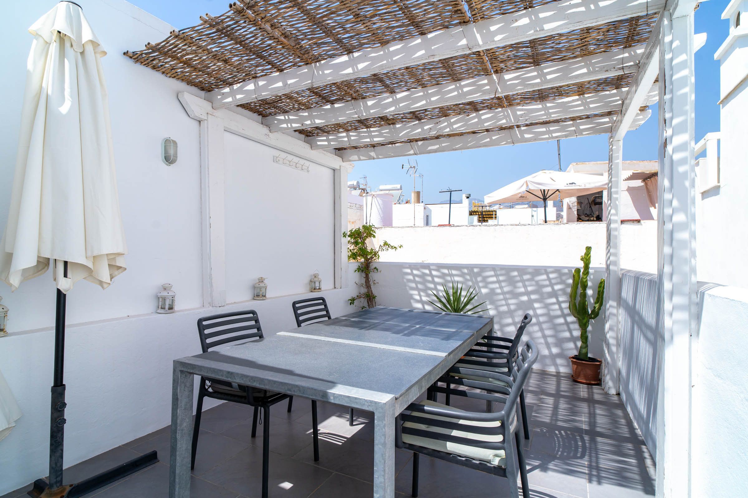 A covered outdoor dining area with a table and chairs, a potted plant, and a white umbrella.