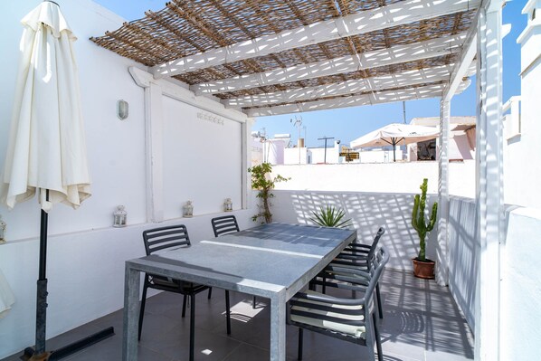 A covered outdoor dining area with a table and chairs, a potted plant, and a white umbrella.