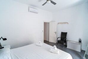 A hotel room with a bed, a chair, a desk with a chair, an iron, and a ceiling fan.