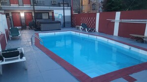 Une piscine rectangulaire bordée de rouge, entourée d’une terrasse en béton. On y trouve des chaises longues et un banc près de la piscine.