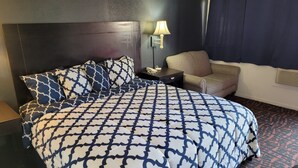 Une chambre d’hôtel avec un grand lit, une chaise, une table de chevet et une lampe.
