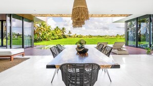 A modern dining area with a large table, black wicker chairs, and a hanging light fixture. - Green Flow Villa 21 (Ubud)