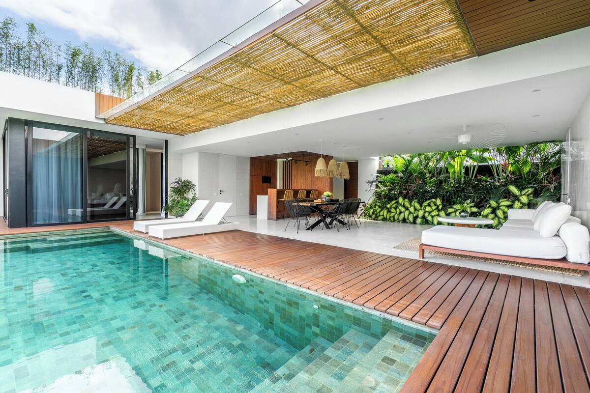 A modern outdoor pool area with a wooden deck, a lounge chair, and a dining area with a table and chairs.
